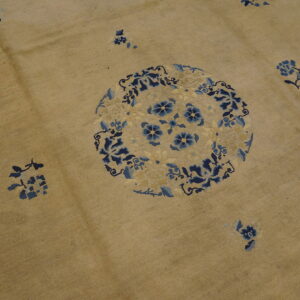 Tan rug featuring a large circular floral medallion and scattered sprays patterned in dark and light blue.