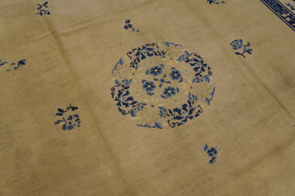 Tan rug featuring a large circular floral medallion and scattered sprays patterned in dark and light blue.