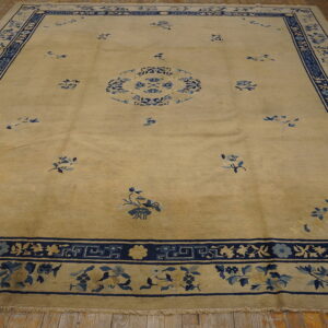 Pale gold area rug featuring a blue floral medallion and detailed blue borders on wood flooring.