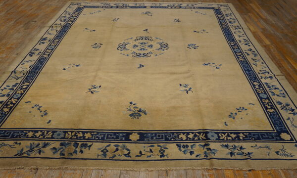 Pale gold area rug featuring a blue floral medallion and detailed blue borders on wood flooring.