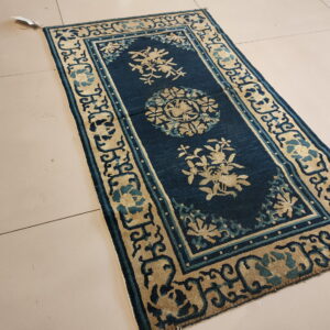 Narrow deep blue rug featuring beige floral medallions and ornate borders rests on light tile floor.