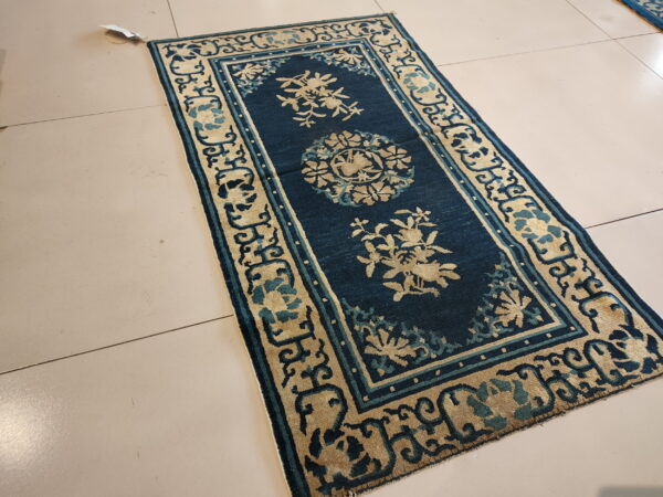 Narrow deep blue rug featuring beige floral medallions and ornate borders rests on light tile floor.