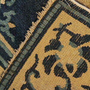 Navy, teal, and tan patterned rug close-up showing high pile texture, fringe, and a woven flat border.