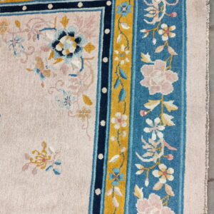 Pink floral rug detail with a plush, ornate border featuring teal, navy, and gold accents.