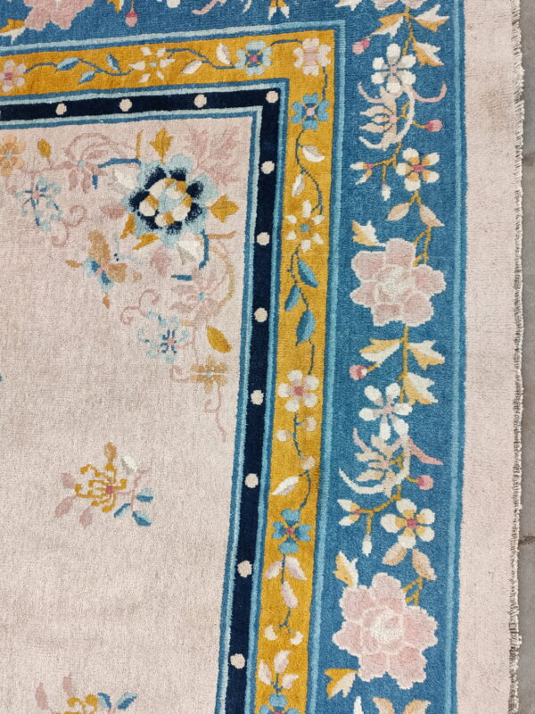Pink floral rug detail with a plush, ornate border featuring teal, navy, and gold accents.