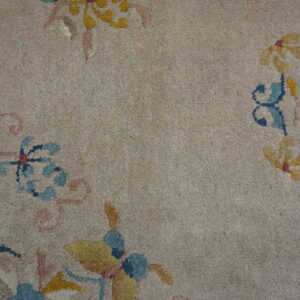 Beige low-pile rug featuring stylized blue, yellow, and pink floral patterns near a dark border.
