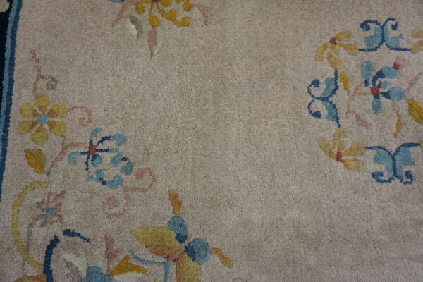 Beige low-pile rug featuring stylized blue, yellow, and pink floral patterns near a dark border.