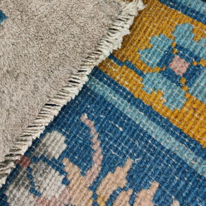 Shaggy beige pile overlaps patterned flatweave featuring blue, yellow, and pink geometric designs and fringe.
