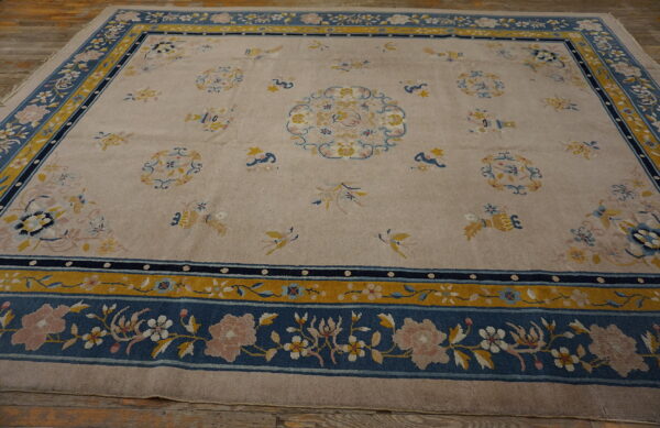 Beige rug with wide blue and gold borders, featuring floral and bird motifs in pink and yellow on a wood floor.