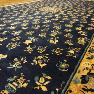 Navy blue rug with gold and teal floral patterns and wide gold border resting on light wood flooring.