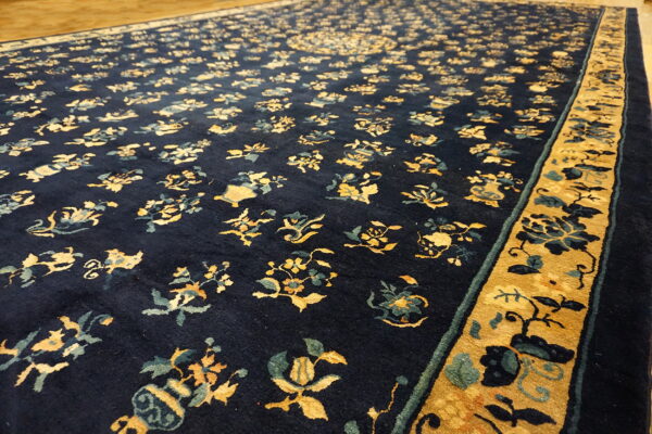 Navy blue rug with gold and teal floral patterns and wide gold border resting on light wood flooring.
