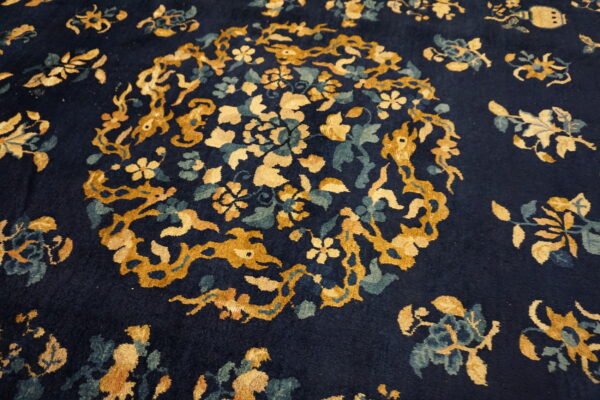 Close-up of a navy rug showing a central gold and teal floral medallion and vines.