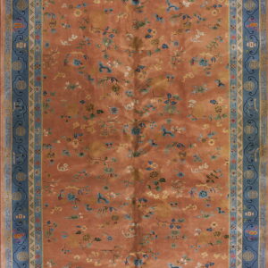 Orange-rust rug with scattered blue and yellow florals, framed by wide borders of ornate slate blue.