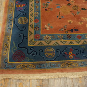 Burnt orange rug with deep blue borders and symbolic floral motifs lies on distressed wood planks.