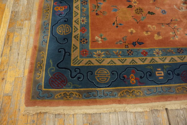 Burnt orange rug with deep blue borders and symbolic floral motifs lies on distressed wood planks.