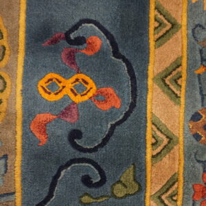 High-pile rug detail showing geometric and floral patterns within teal, gold, tan, and rust colored vertical stripes.