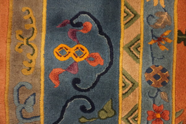 High-pile rug detail showing geometric and floral patterns within teal, gold, tan, and rust colored vertical stripes.