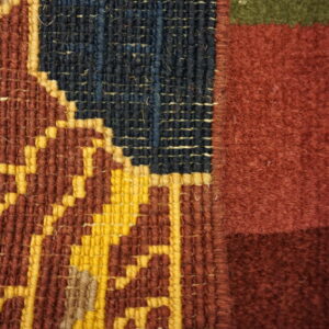 Woven rug detail featuring distinct flatweave geometry in yellow and red transitioning to a solid maroon pile.