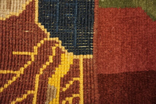 Woven rug detail featuring distinct flatweave geometry in yellow and red transitioning to a solid maroon pile.
