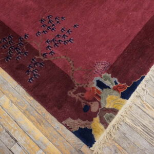 The maroon rug features a multicolored stylized tree pattern and fringe against worn wood flooring.