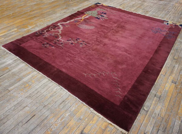 Rectangular magenta rug with scenic branch patterns and a dark border rests on worn wood planks.