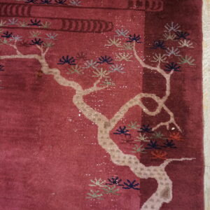 A deep red rug with a light-colored stylized tree design lies on distressed gray and yellow wood planks.