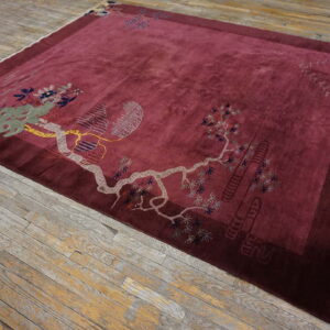 Plush maroon rug with light gray and green botanical designs rests on rustic, worn wood flooring.