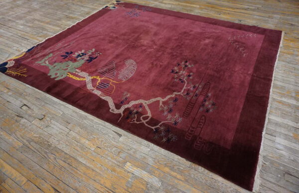 Plush maroon rug with light gray and green botanical designs rests on rustic, worn wood flooring.