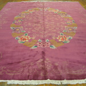 Magenta rug with a colorful floral oval medallion, subtle light pink field motifs, and white fringe on wood planks.