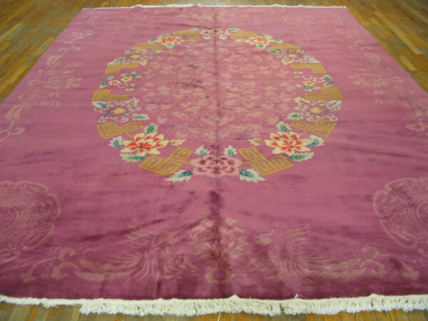 Magenta rug with a colorful floral oval medallion, subtle light pink field motifs, and white fringe on wood planks.