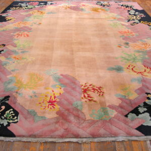 Peach high-pile rug featuring a border of black, pink herringbone, and colorful stylized floral designs on wood flooring.