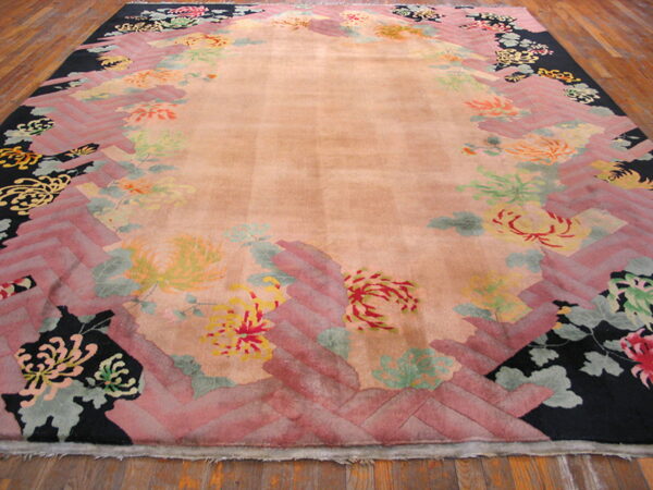 Peach high-pile rug featuring a border of black, pink herringbone, and colorful stylized floral designs on wood flooring.