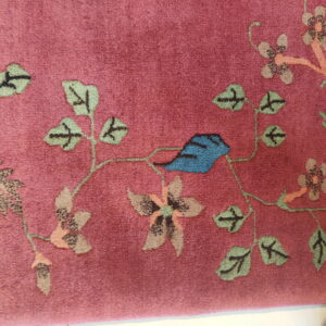 Plush magenta rug displays a border of green vines, tan flowers, and a partial blue bird.