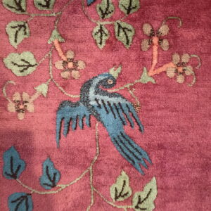 Magenta cut-pile rug detail showing a blue bird and stylized pink and green botanical patterns.