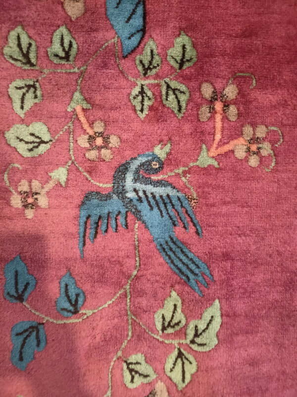 Magenta cut-pile rug detail showing a blue bird and stylized pink and green botanical patterns.