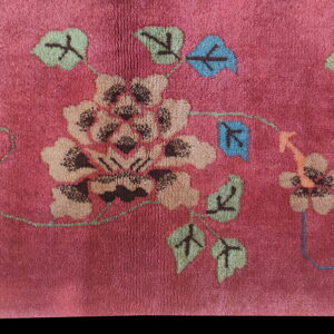 Deep pink, plush rug detail featuring a stylized floral and vine pattern in tan, blue, and green.