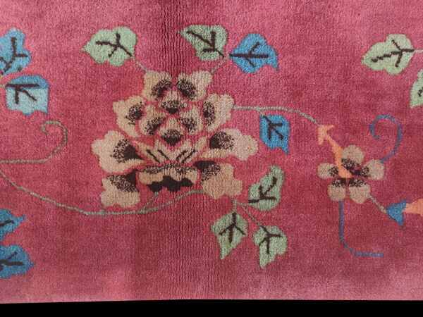 Deep pink, plush rug detail featuring a stylized floral and vine pattern in tan, blue, and green.