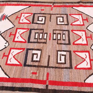 Southwestern geometric flat weave rug in red, white, brown, and tan on rustic wood planks.