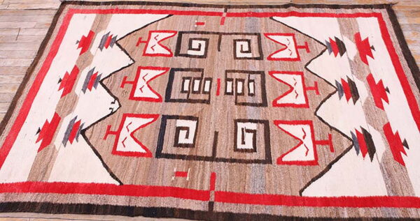 Southwestern geometric flat weave rug in red, white, brown, and tan on rustic wood planks.