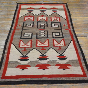 Geometric red, black, and neutral-toned rug with stepped designs and abstract figures on worn wood flooring.