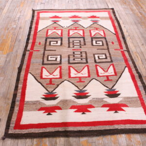Geometric flat-weave rug in red, brown, and cream sits on rustic wide-plank wood flooring.