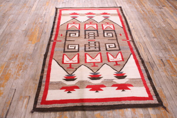 Geometric flat-weave rug in red, brown, and cream sits on rustic wide-plank wood flooring.