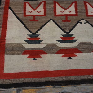 Geometric flatweave rug featuring red, white, brown, and black symbols resting on rustic wood flooring.