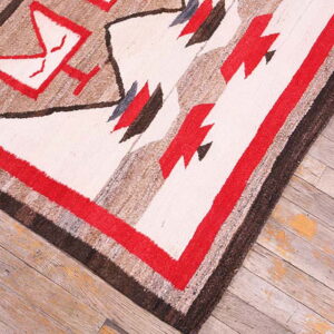 Textured geometric rug featuring white, red, tan, and dark brown designs on worn wood planks.