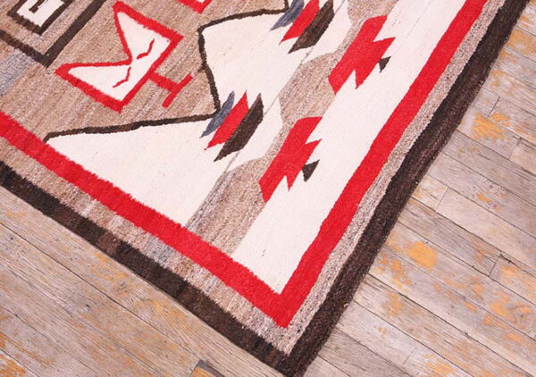 Textured geometric rug featuring white, red, tan, and dark brown designs on worn wood planks.