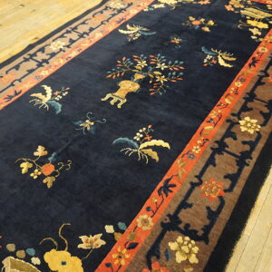 Navy blue rug with multicolored stylized floral motifs and thick contrasting borders rests on light wood flooring.