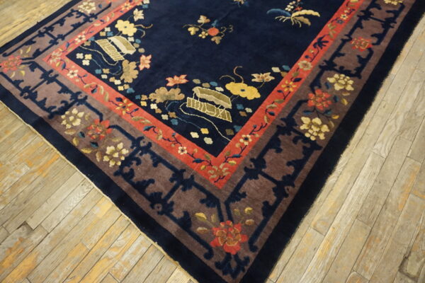 Plush navy rug with floral motifs and borders in brown and terracotta, resting on light wood planks.