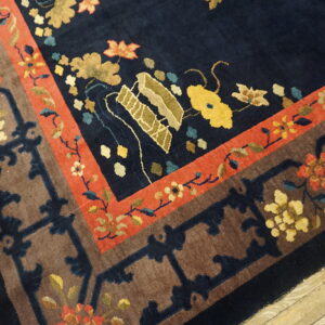 Ornate navy blue rug with stylized flowers and geometric brown and red borders shown on rustic wood planks.