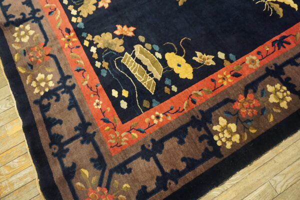Ornate navy blue rug with stylized flowers and geometric brown and red borders shown on rustic wood planks.