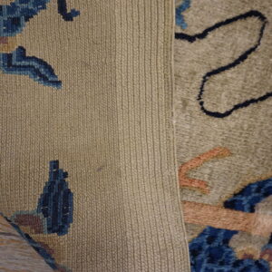 A rug with a plush tan and blue pattern is rolled back, showing its tightly ribbed woven backing on wood flooring.